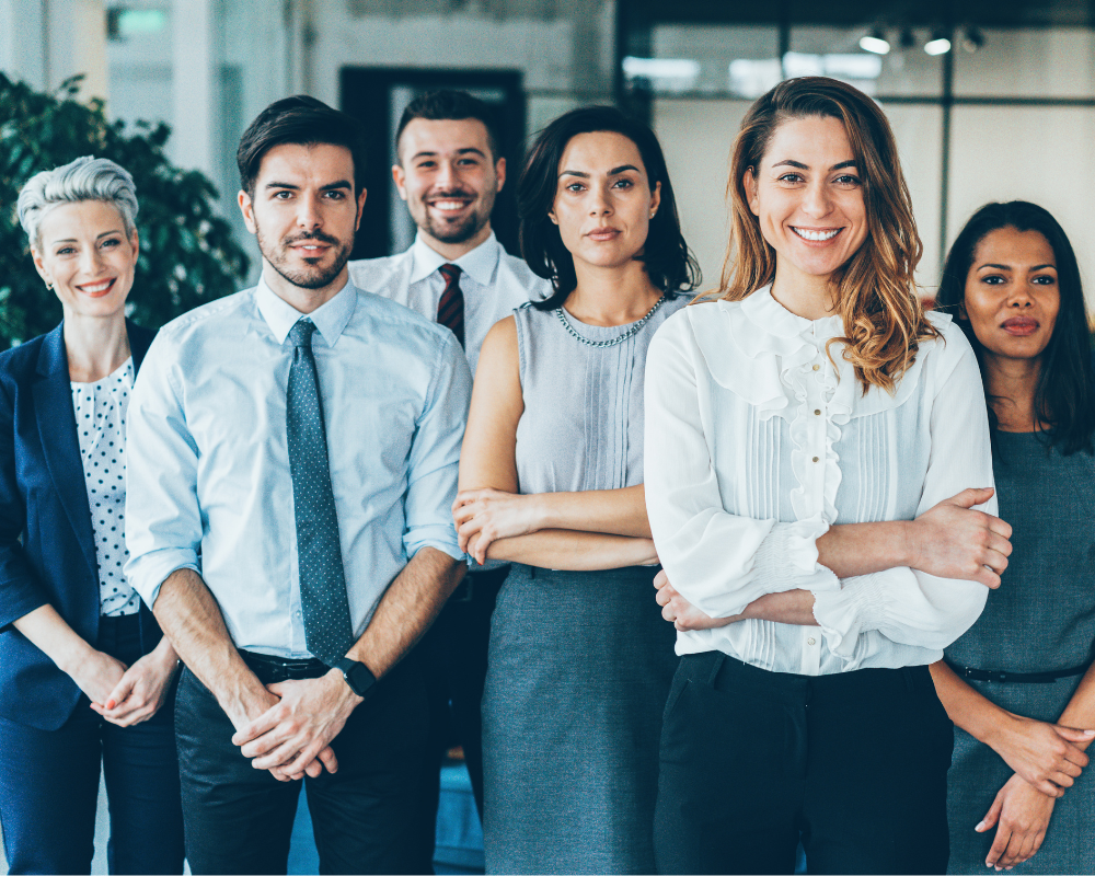 Six professionals in business attire standing together, smiling and looking confident.