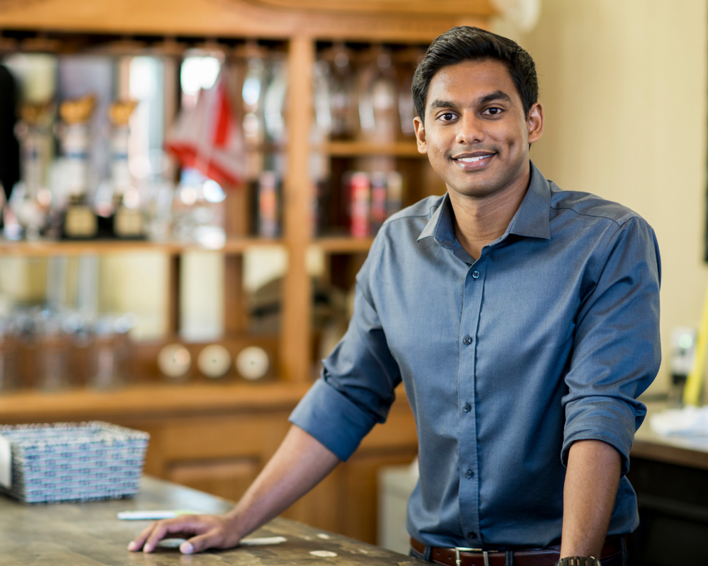 Young businessman standing at a bar counter, smiling confidently at the camera.