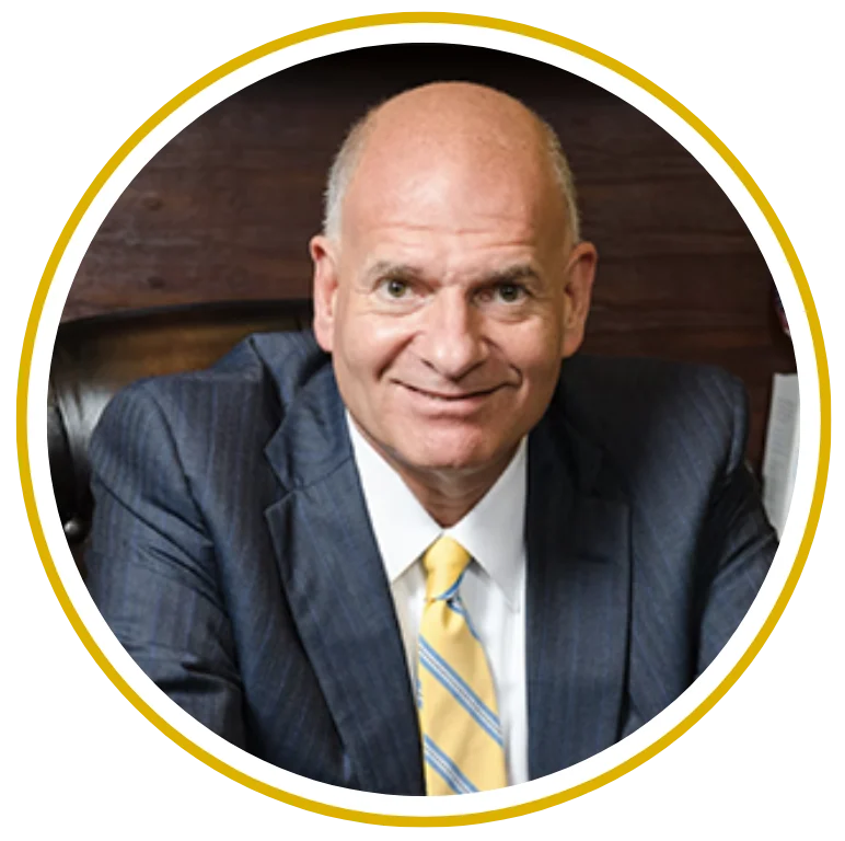 Professional man in a blue suit and yellow tie, seated and smiling at the camera.