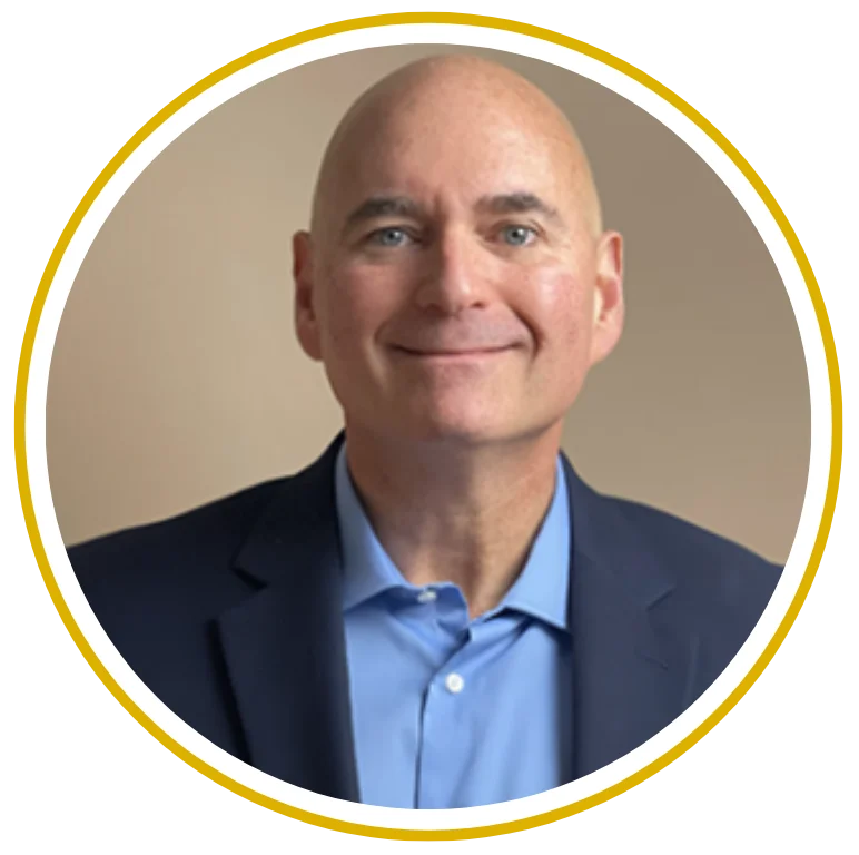 Professional man with a shaved head wearing a blue suit and light blue shirt, smiling at the camera.