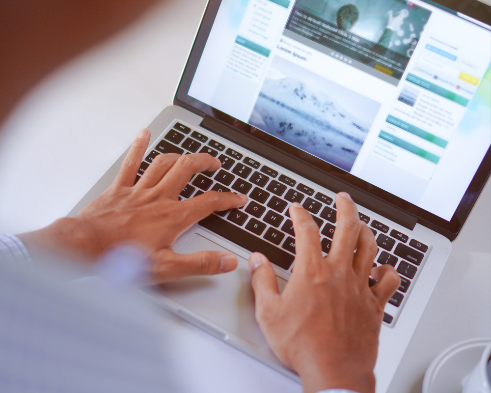 Close-up of hands typing on a laptop keyboard with a website open on screen.