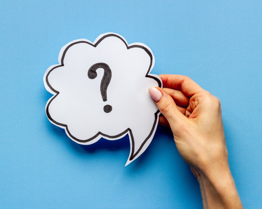 Hand holding a paper cutout shaped like a speech bubble with a question mark inside.