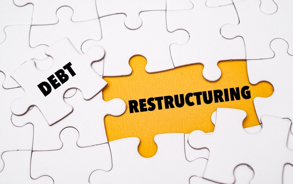 Jigsaw puzzle pieces labelled Debt and Restructuring fitting together against an orange background