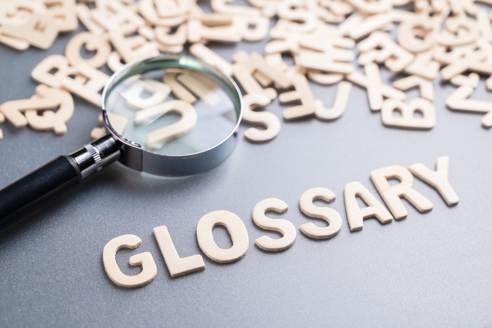 Wooden letters spelling the word "GLOSSARY" next to a magnifying glass on a grey background.