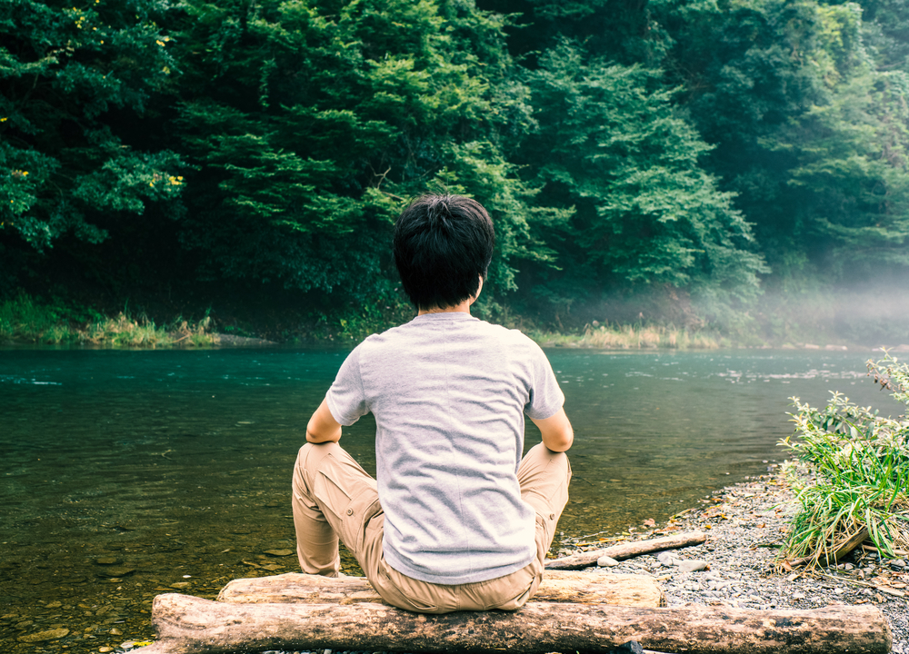 • Man meditating on a log next to a peaceful river.